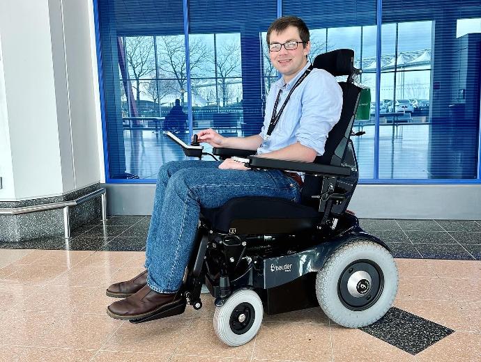 A white male wearing jeans, a pale blue shirt and glasses. He is sitting in a rear wheel drive Balder Liberty L380 and smiling at the camera.