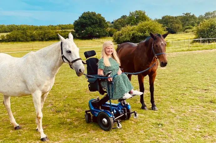 Anna, sitting in her blue Balder F380, in a field with 2 horses