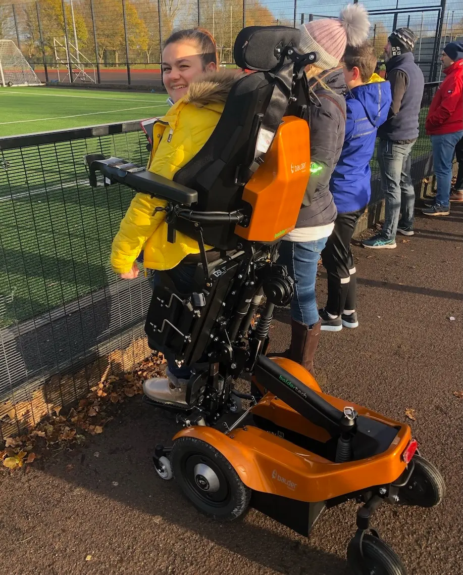 Franchesca, standing in her Balder F390 standing powerchair at the edge of a football pitch